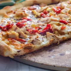 Pyszna pizza włoska z kurczakiem i suszonymi pomidorami, z chrupiącym brzegiem, na kamieniu do pieczenia.