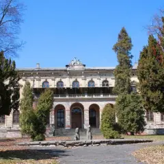 Dawny pałac, otoczony drzewami, z widoczną **promną** fasadą i arkadowym wejściem.