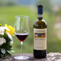 Un bicchiere di Brunello di Montalcino, un vino pregiato, accanto a un bouquet di fiori e una bottiglia CastelGiocondo.
