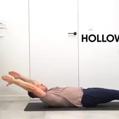 Mężczyzna leży na macie, wykonując ćwiczenie hollow body. Ręce wyciągnięte nad głowę, nogi uniesione.