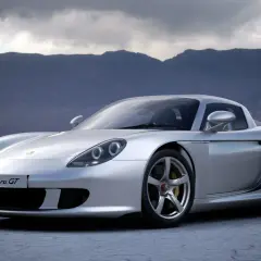 Srebrny Porsche Carrera GT na pustkowiu, z górami w tle.