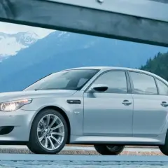 Un elegante BMW M5 E60 plateado descansa ante un paisaje montañoso nevado, listo para la aventura.