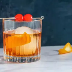 Klasyczny koktajl z pomarańczową skórką, lodem i dwiema wiśniami na patyczku. Idealny old fashioned przepis.