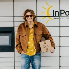 Uśmiechnięty mężczyzna z paczką InPost przy automacie. Zbliża się godzina graniczna nadania, ale on jest gotowy.