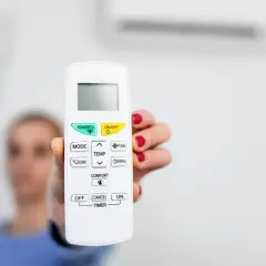 Mano sostiene control remoto de aire acondicionado, listo para activar el símbolo del frío y disfrutar de un ambiente fresco.