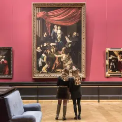 Dwie kobiety oglądają obrazy w muzeum sztuki na tle czerwonej ściany.