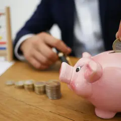 Różowa świnka skarbonka, monety, liczydło i ręka wrzucająca monetę.