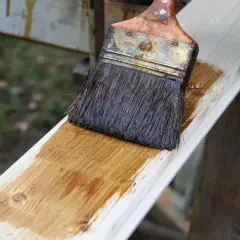 Application d'une lasure blanche sur une planche de bois. Le résultat avant/après est visible sur la surface traitée.