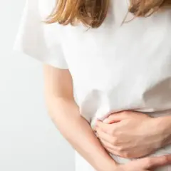 Donna con le mani sull'addome, che esprime disagio e difficoltà a digerire.