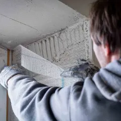Hand mit Handschuh verputzt Fensterlaibung mit Armierungsgewebe.