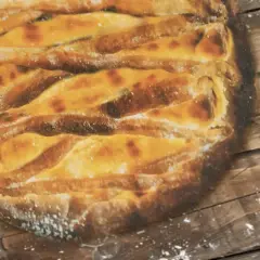 Une tarte au libouli dorée, aux croisillons de pâte bien cuits, repose sur un fond de bois rustique saupoudré de farine.