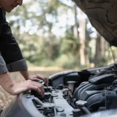 Un homme regarde le moteur de sa voiture qui cale à bas régime, bloqué en pleine nature.