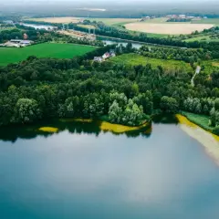 Malowniczy krajobraz z lasem i polami otaczającymi najczystsze jezioro w Polsce. W oddali widać zabudowania i kanał.