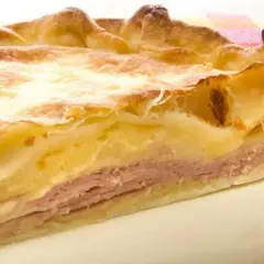 Rebanada de tarta de jamón y queso, con capas de masa dorada, jamón rosado y relleno cremoso. ¡Un bocado delicioso!