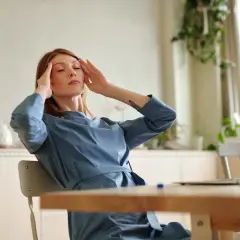 Mujer con dolor de cabeza lado izquierdo, se masajea las sienes con los ojos cerrados.