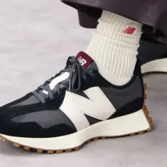 Sznurowanie butów New Balance. Ciemne sneakersy z białym logo N i brązową podeszwą.
