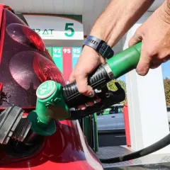 Remplissage d'une voiture thermique rouge à la station-service. Le pistolet vert est inséré dans le réservoir.