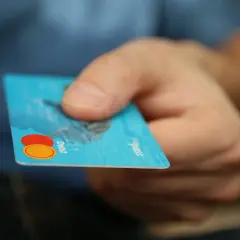 Main d'une personne tenant une carte bancaire bleue. L'inconvénient d'une carte à autorisation systématique est qu'elle peut être refusée si le solde est insuffisant.