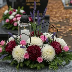 Wiosenne bukiety na grobie: białe i bordowe chryzantemy, różowe róże, lawenda i świeca.