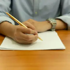 Main tenant une plume dorée, une personne rédige une lettre de motivation STAPS sur une feuille blanche.