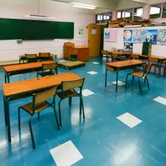 Pusta klasa szkolna z rzędami drewnianych ławek i krzeseł na niebieskiej podłodze.