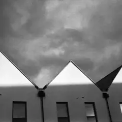Row of modern houses with sharp, triangular roofs against a dramatic, cloudy sky. The light creates a stark contrast, highlighting the architectural lines, a testament to careful stand development.