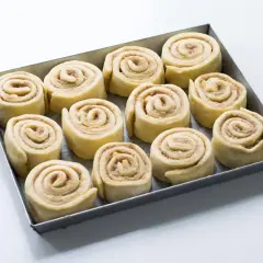 Rotolini alla cannella e mela pronti per essere infornati, disposti in una teglia.