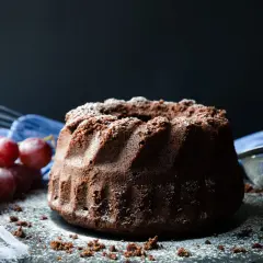 En saftig sockerkaka choklad, pudrad med florsocker, med vindruvor och visp i bakgrunden.