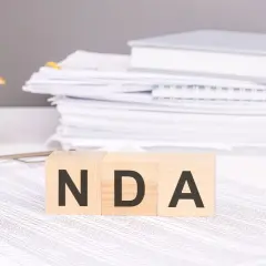 Cubos de madera con las letras NDA, una casa de juguete y pilas de documentos.