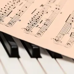Partytura muzyczna z nutami, leżąca na klawiaturze fortepianu. Melodia w stylu barokowym czeka na wykonanie.