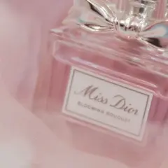 Frasco de perfume Miss Dior Blooming Bouquet, con un lazo plateado, sobre tela rosa suave. Un toque de elegancia para la madame de rosa.