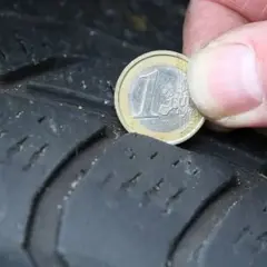Nahaufnahme eines Reifens, auf dem eine 1-Euro-Münze zur Messung der Profiltiefe liegt.