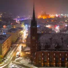 Nocna panorama Kościerzyny, ośnieżona trasa miejska z kościołem w centrum i rozświetlonymi budynkami.