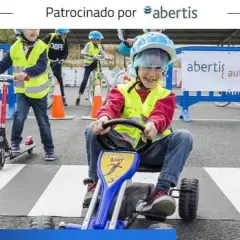 Niños aprenden seguridad vial en actividades educativas. Un niño en un kart, otro en patinete y otros en bicicleta, todos con chalecos reflectantes.