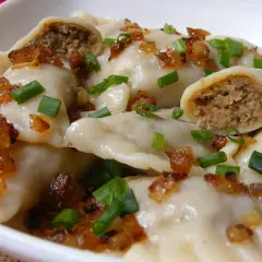 Pyszne pierogi z mięsem, posypane skwarkami i szczypiorkiem, kuszą swoim wyglądem.
