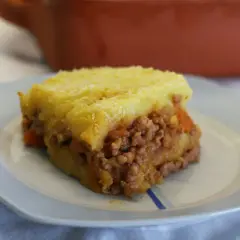 Un trozo de pastel de carne tradicional con puré de patatas gratinado, servido en un plato azul claro.