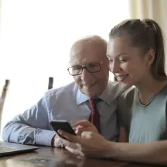 Starszy mężczyzna i młoda kobieta patrzą na telefon, uśmiechając się.