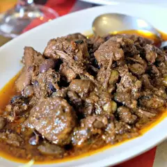 Un saporito cinghiale alla cacciatora, con olive e una ricca salsa, servito in un piatto bianco.