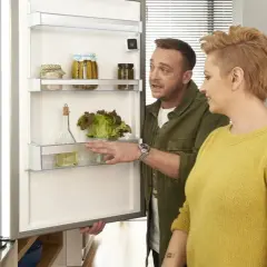 Para wybrać jaką lodówkę wybrać, para ogląda wnętrze z sałatą i przetworami.
