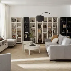 Nowoczesny living room z szarą sofą, regałami pełnymi książek i dekoracji, okrągłym stolikiem kawowym i lampą łukową.