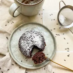 Ein saftiger Schokoladen-Tassenkuchen ohne Ei, bestäubt mit Puderzucker und Schokostreuseln, wartet auf dem Teller.