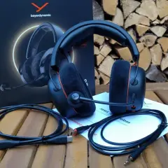 Beyerdynamic MMX 150 Test: Gaming-Headset mit Mikrofon, Kabeln und Anleitung auf Holztisch vor Holzstapel.