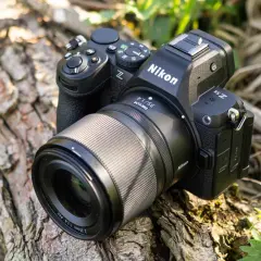 Aparat Nikon Z5 II z obiektywem Nikkor 35mm f/1.4 leży na spróchniałym drewnie, otoczony zielenią.