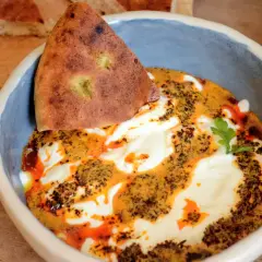 Un bol de cilbir recette, avec du pain pita trempé dans une sauce crémeuse et épicée, garni d'herbes fraîches.