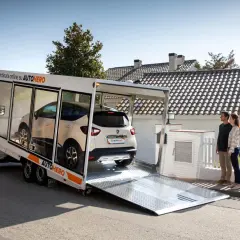 Coppia attende la consegna della sua nuova auto, ordinata online su AUTOhero Italy, scaricata da un bisarca.