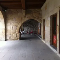 Arcadas de piedra en el casco antiguo de Galicia, con mesas y sillas de exterior. Los muros de piedra transmiten la historia de la zona.