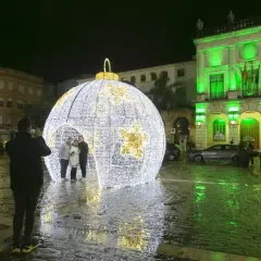 Una gran bola de luces ilumina la plaza en esta nit de cap d'any. Gente se hace fotos junto a la decoración.