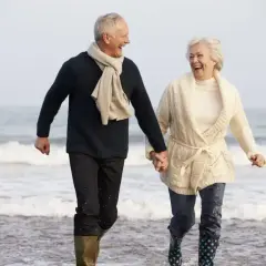 Szczęśliwa para seniorów biegnie plażą, trzymając się za ręce. Idealne tanie wycieczki dla seniorów, by poczuć radość życia!