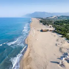 Piękne turcja plaże z turkusową wodą, piaszczystym brzegiem i zielonymi wzgórzami w tle. Rząd leżaków zaprasza do odpoczynku.