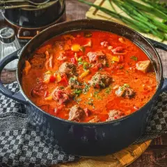 Herzhaftes Pfundstopf Rezept in einem Gusseisentopf, mit Fleischklößchen, Paprika und einer würzigen Tomatensoße, garniert mit frischen Kräutern.